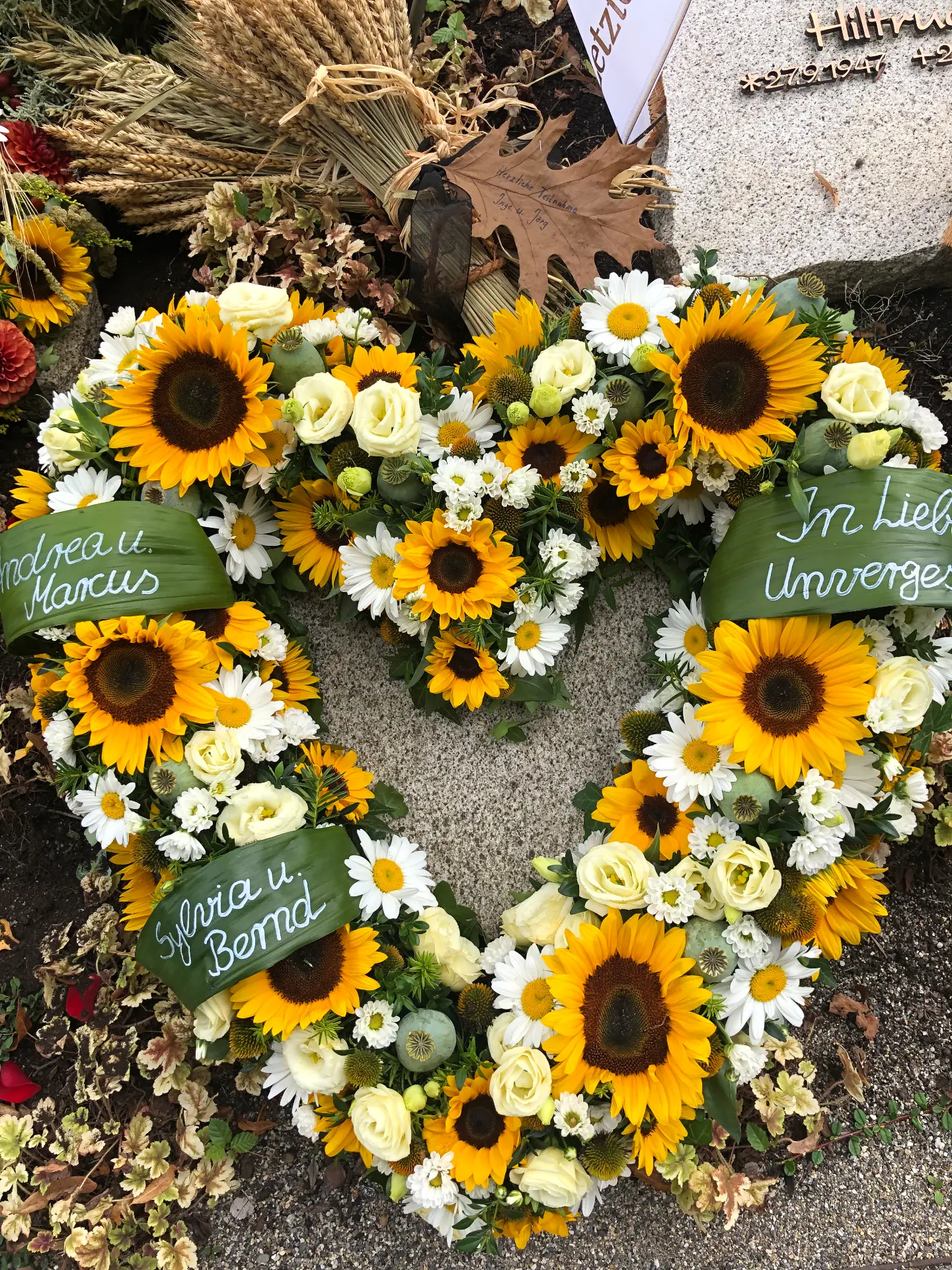 Herzförmiger Trauerkranz mit Sonnenblumen, weißen Rosen und Margeriten