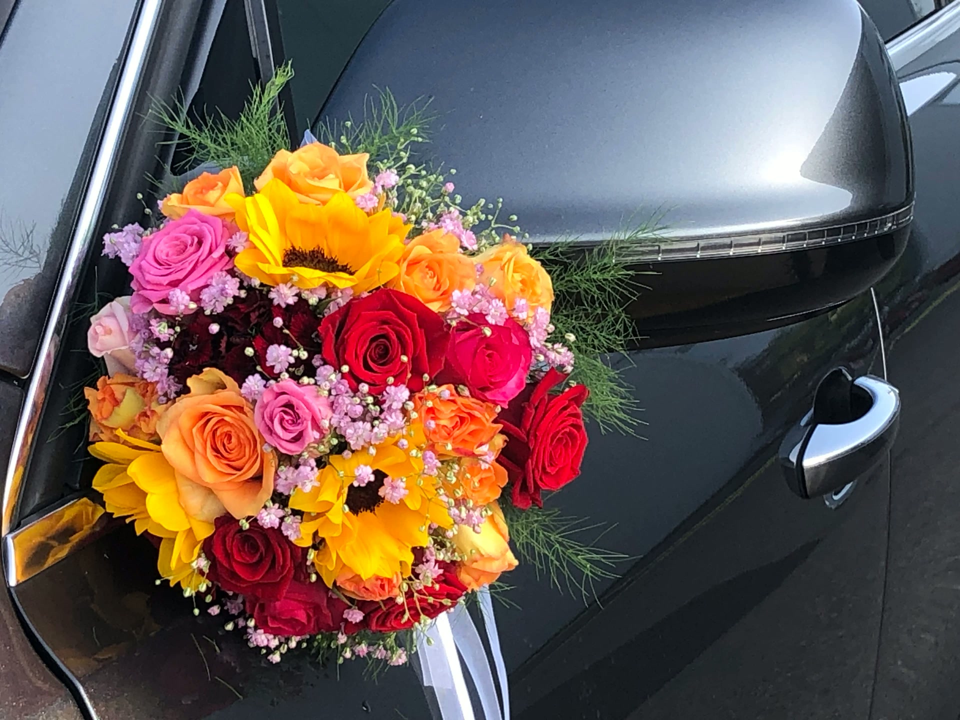 Bunter Strauß mit Rosen, Sonnenblumen und Schleierkraut am Außenspiegel eines Autos