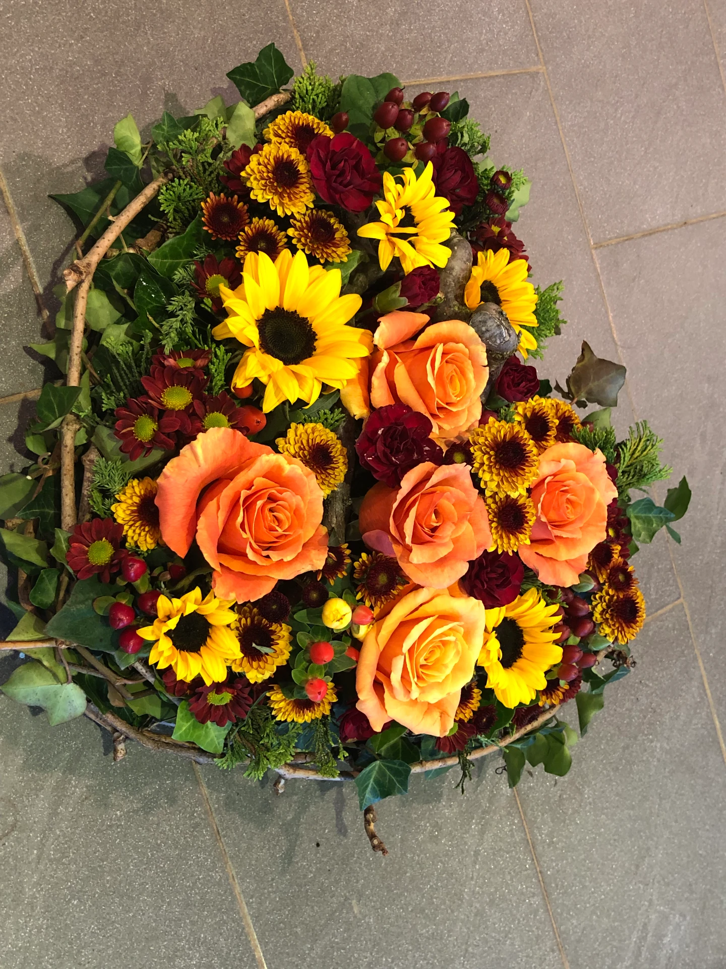Trauergesteck mit orangefarbenen Rosen, Sonnenblumen und dunklen Chrysanthemen