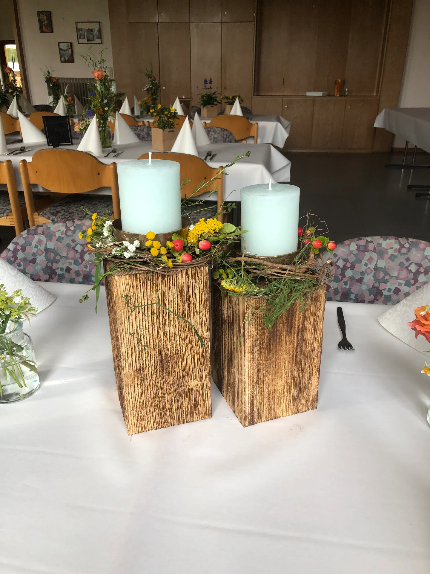 Festliche Tischdekoration mit hellen Kerzen auf Holzblöcken, umkränzt von Wiesenblumen und Hagebutten