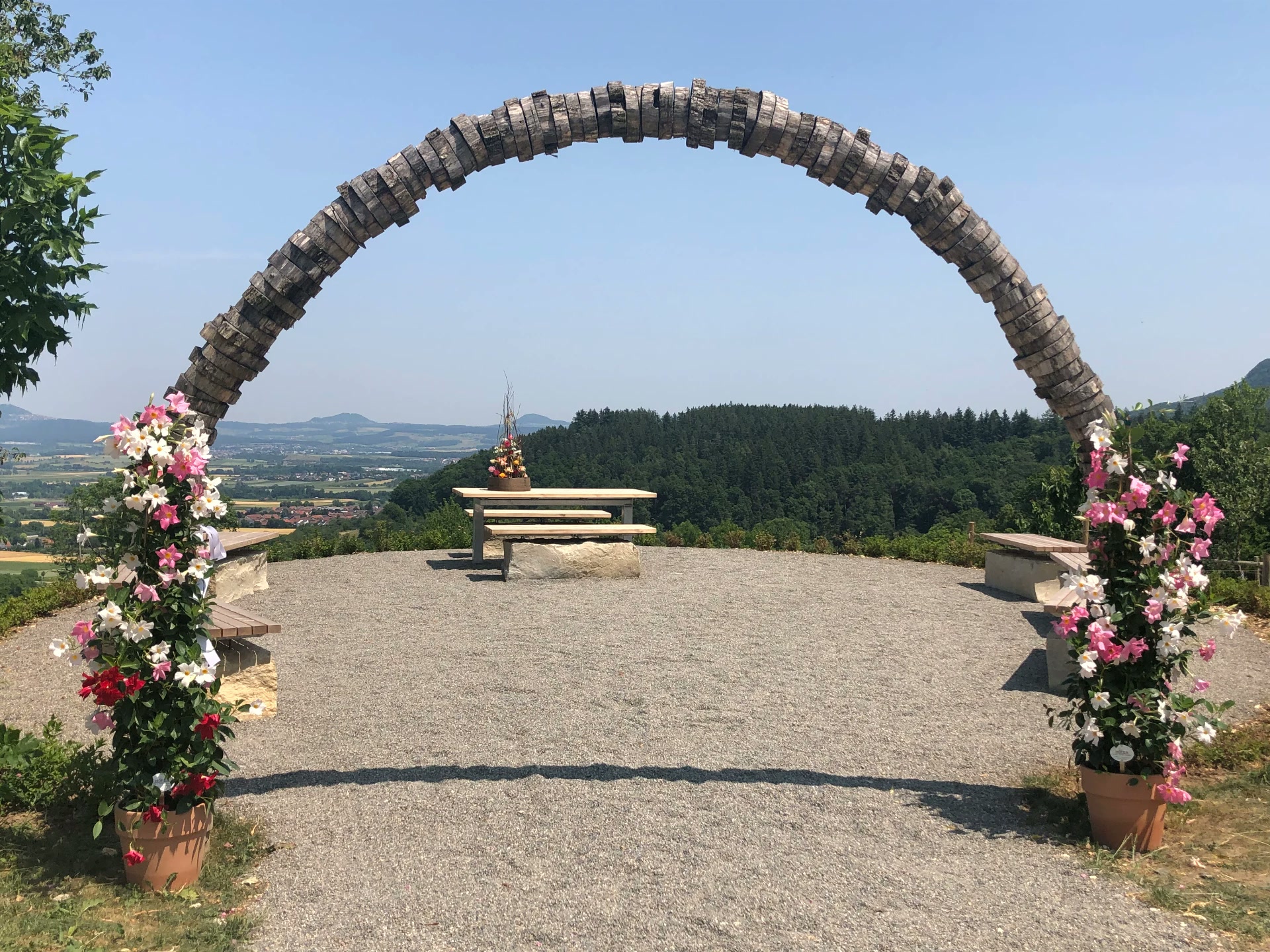 Festplatz mit großem geschwungenem Holzbogen und blühenden Blumen in Übertöpfen