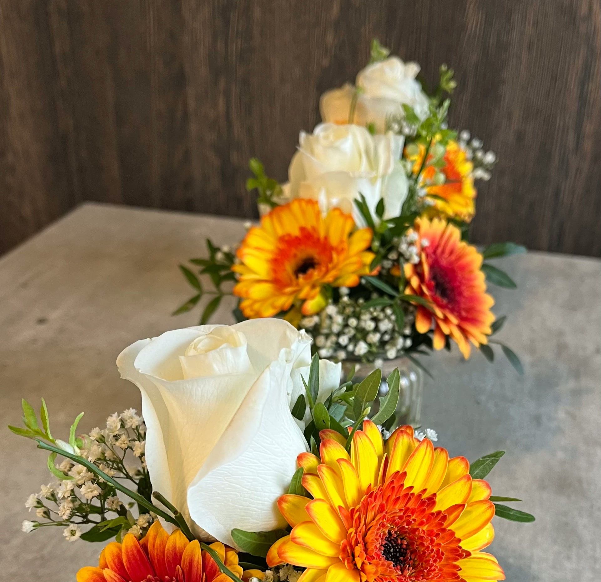 Sträuße mit weißen Rosen und orange-roten Gerbera in Glasvasen